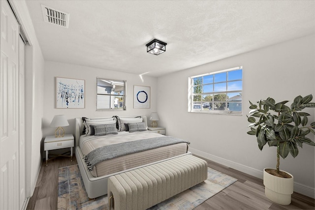 bedroom featuring visible vents, baseboards, a textured ceiling, and wood finished floors