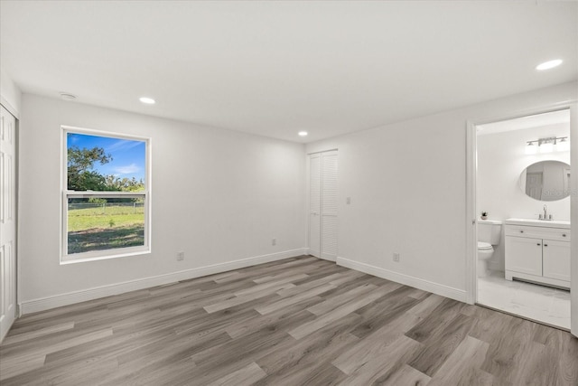 unfurnished bedroom with recessed lighting, light wood-style floors, baseboards, and ensuite bathroom