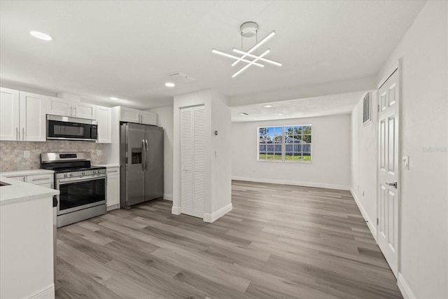 kitchen with light wood-type flooring, stainless steel appliances, white cabinets, light countertops, and decorative backsplash