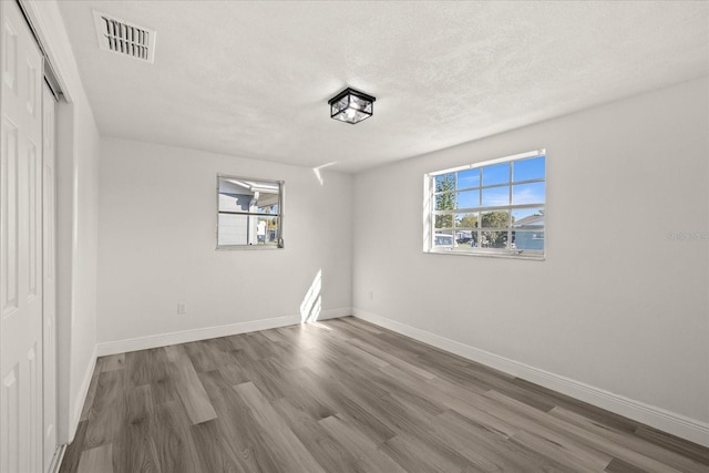 unfurnished room with visible vents, baseboards, a textured ceiling, and wood finished floors