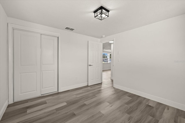 unfurnished bedroom with a closet, visible vents, baseboards, and wood finished floors