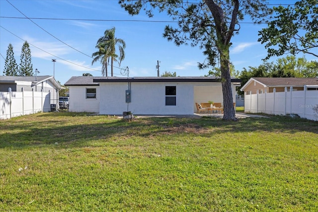 back of house with stucco siding, a lawn, and fence