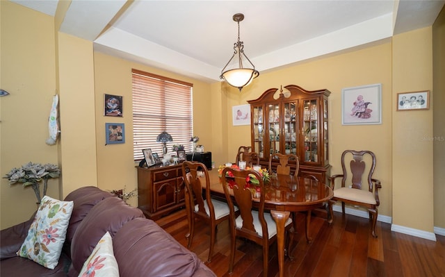 dining space with a tray ceiling, baseboards, and dark wood-style floors