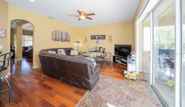 living area with visible vents, baseboards, ceiling fan, wood finished floors, and arched walkways