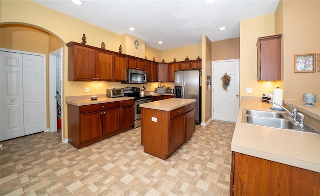 kitchen featuring a center island, light countertops, appliances with stainless steel finishes, arched walkways, and a sink