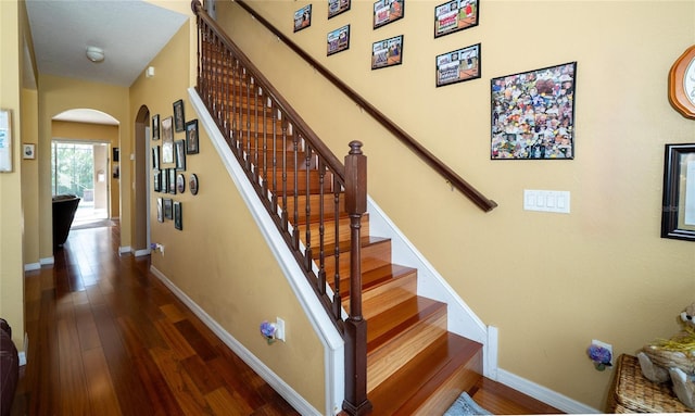 stairs with baseboards, arched walkways, and hardwood / wood-style floors