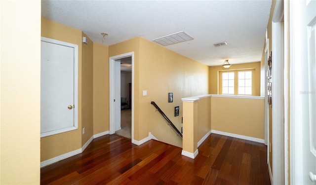 hallway featuring wood finished floors, an upstairs landing, visible vents, and baseboards