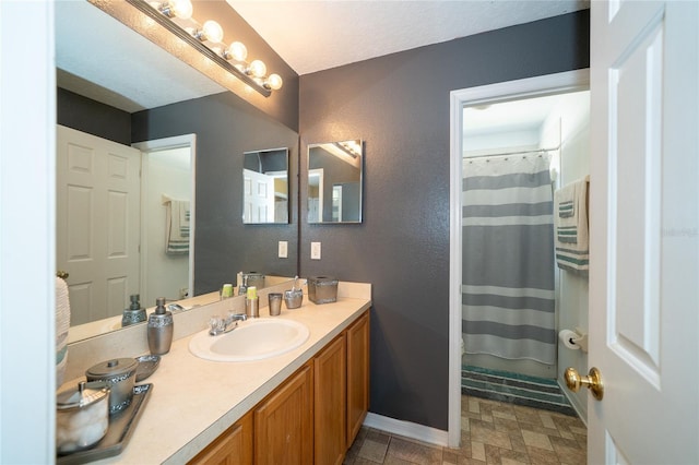 bathroom with stone finish floor, vanity, a shower with shower curtain, and baseboards