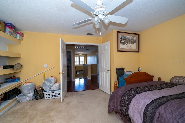 bedroom featuring a textured ceiling, ceiling fan, visible vents, and light carpet