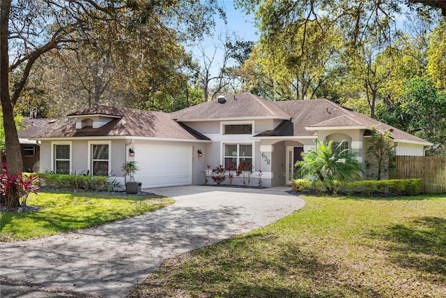 view of front facade with stucco siding, driveway, fence, a front yard, and a garage