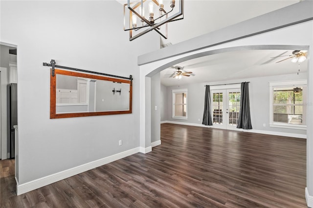 unfurnished living room with baseboards, dark wood-style flooring, arched walkways, french doors, and ceiling fan with notable chandelier