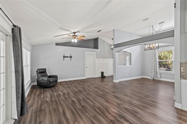 unfurnished living room with vaulted ceiling, dark wood-style floors, ceiling fan with notable chandelier, and arched walkways