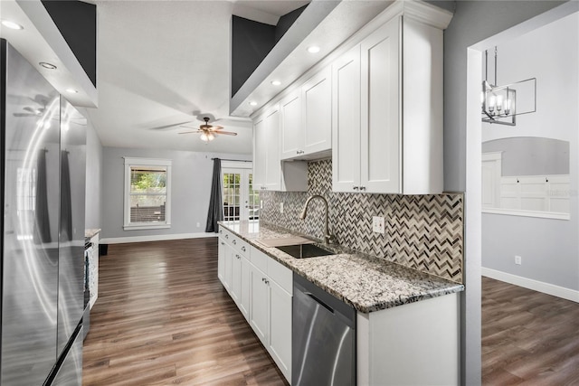 kitchen with dark wood-style floors, a sink, stainless steel appliances, ceiling fan with notable chandelier, and backsplash