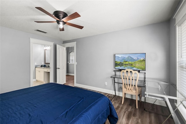 bedroom featuring visible vents, ceiling fan, baseboards, ensuite bathroom, and wood finished floors