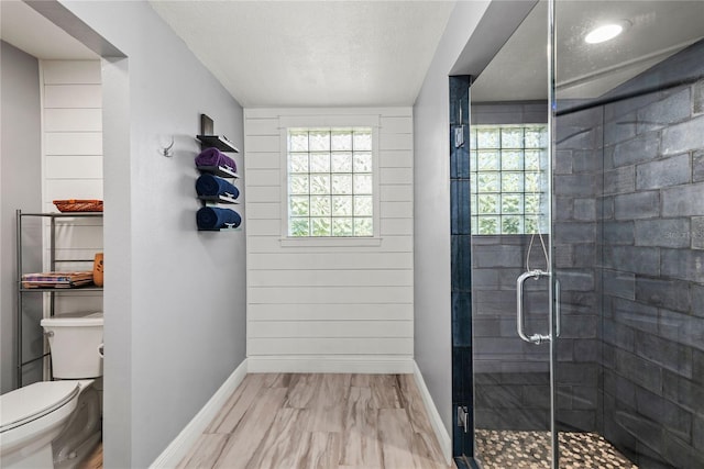 bathroom featuring toilet, plenty of natural light, baseboards, and a stall shower