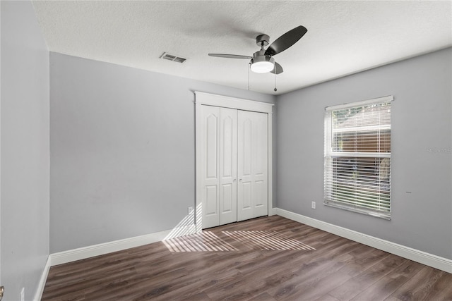 unfurnished bedroom featuring visible vents, a textured ceiling, wood finished floors, a closet, and baseboards