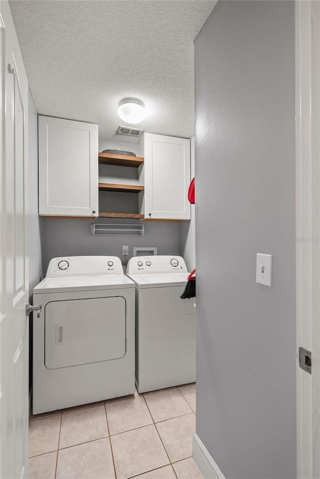 clothes washing area with visible vents, light tile patterned floors, washer and dryer, cabinet space, and a textured ceiling