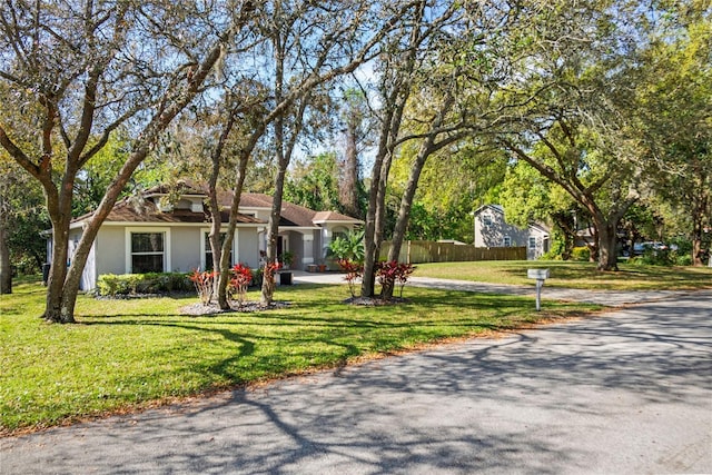 view of front of home with stucco siding, driveway, a front lawn, and fence