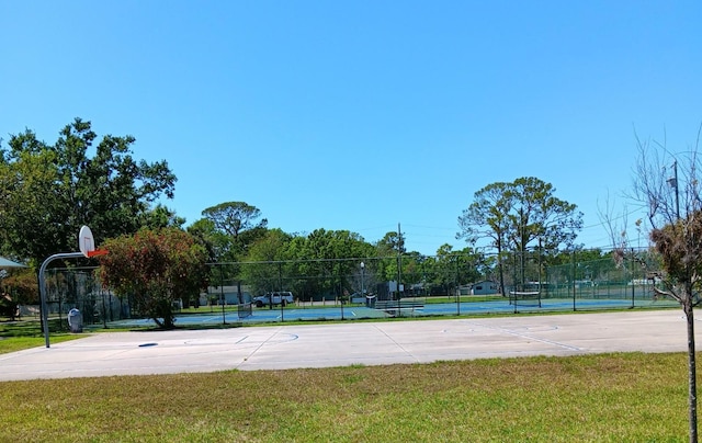 view of sport court featuring a tennis court, community basketball court, a yard, and fence