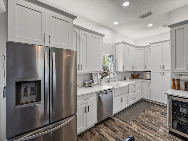 kitchen featuring visible vents, beverage cooler, a sink, stainless steel appliances, and dark wood-style flooring