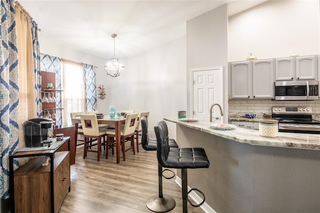 kitchen featuring light stone counters, decorative backsplash, light wood-style flooring, appliances with stainless steel finishes, and a notable chandelier