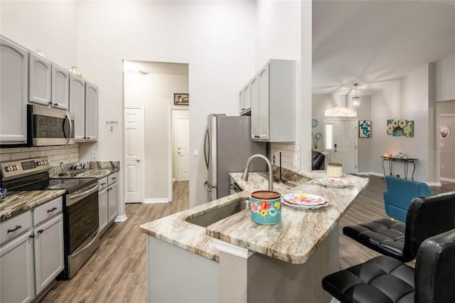 kitchen with backsplash, light stone counters, appliances with stainless steel finishes, a peninsula, and a kitchen breakfast bar