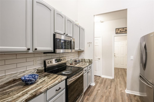 kitchen with light wood finished floors, backsplash, baseboards, light stone countertops, and stainless steel appliances