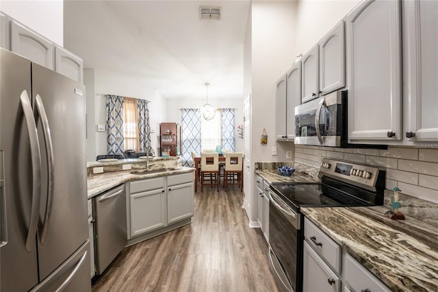 kitchen featuring wood finished floors, visible vents, a sink, decorative backsplash, and appliances with stainless steel finishes