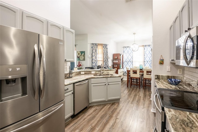 kitchen with light wood-style flooring, a sink, stainless steel appliances, a peninsula, and an inviting chandelier