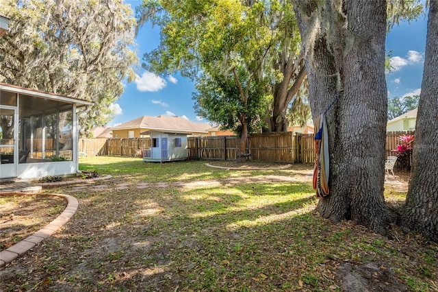 view of yard with an outdoor structure, a storage shed, a fenced backyard, and a sunroom