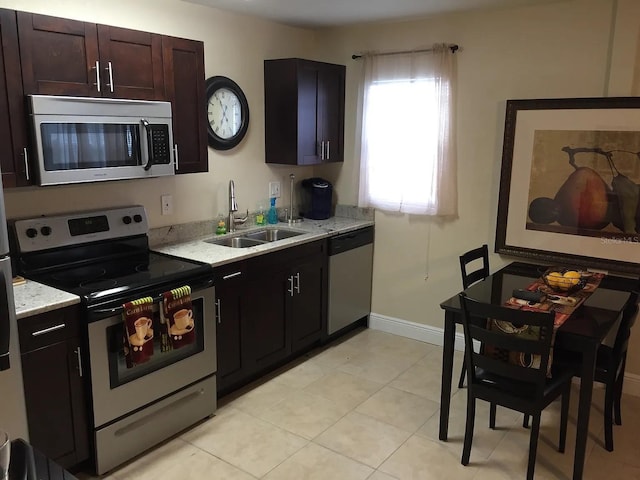 kitchen featuring light stone counters, stainless steel appliances, baseboards, and a sink