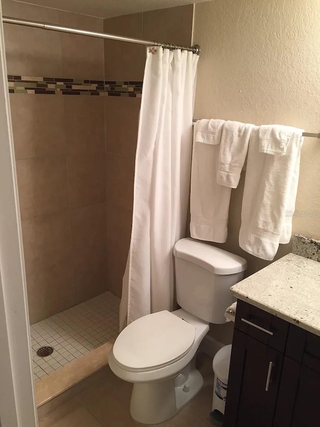 full bathroom featuring a shower stall, toilet, a textured wall, tile patterned floors, and vanity