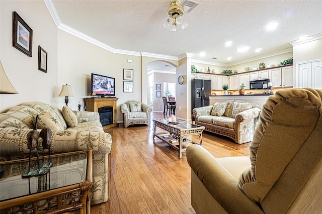 living area featuring visible vents, ornamental molding, light wood-style flooring, arched walkways, and a textured ceiling