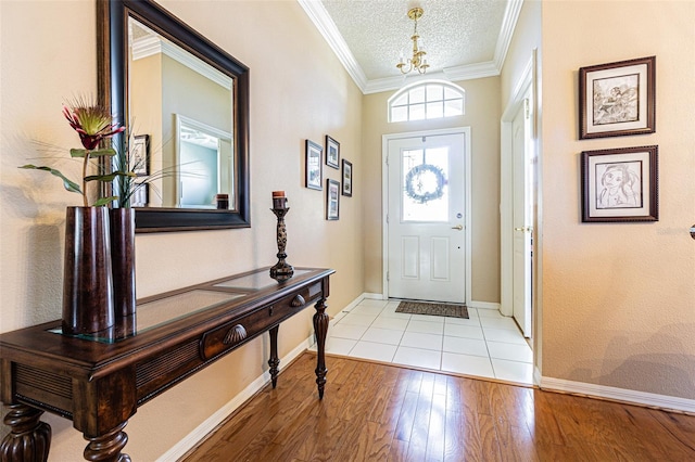 entryway featuring baseboards, a chandelier, light wood-type flooring, ornamental molding, and a textured ceiling