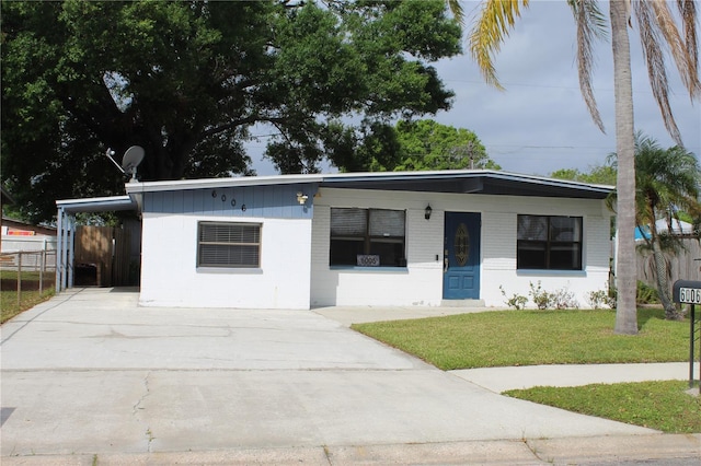 view of front of property featuring an attached carport, concrete block siding, a front yard, fence, and concrete driveway