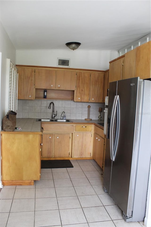 kitchen featuring tasteful backsplash, stainless steel refrigerator with ice dispenser, light tile patterned floors, and a sink