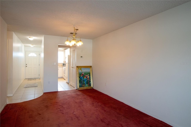 empty room featuring a textured ceiling, a notable chandelier, light tile patterned floors, and light carpet