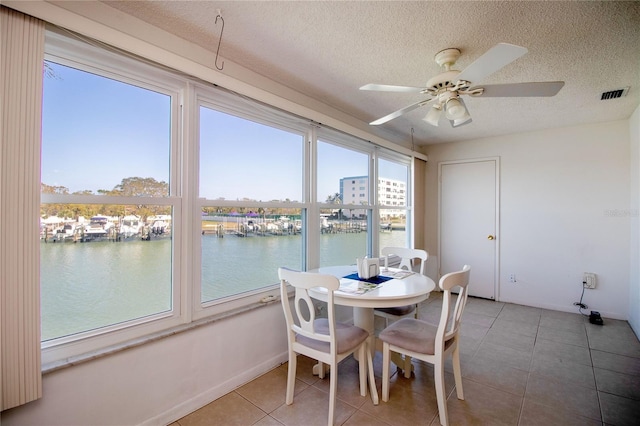 tiled dining room with visible vents, a healthy amount of sunlight, a textured ceiling, and a water view