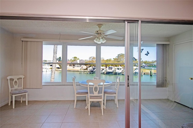 dining room with light tile patterned flooring, a ceiling fan, a water view, and baseboards