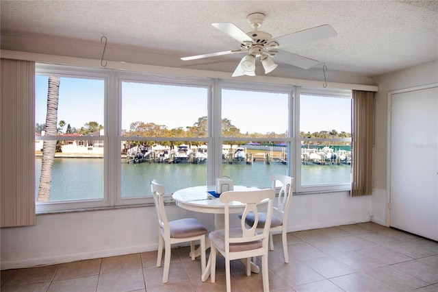 tiled dining room with a textured ceiling, baseboards, a water view, and ceiling fan