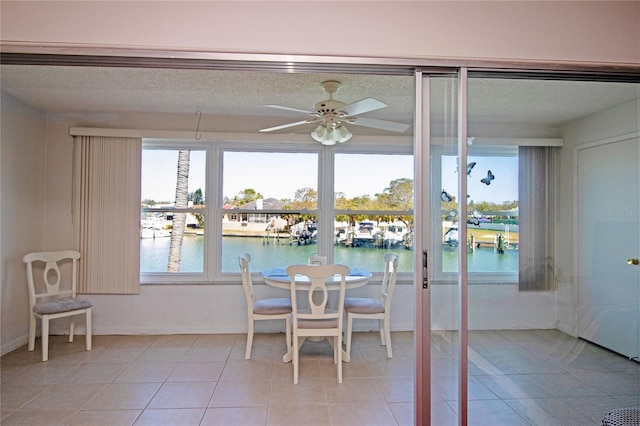 dining room with light tile patterned flooring, a water view, a textured ceiling, and a ceiling fan