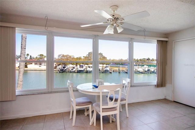 tiled dining space featuring a textured ceiling, a water view, baseboards, and a ceiling fan