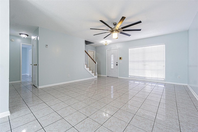 unfurnished living room with baseboards, stairway, light tile patterned flooring, a textured ceiling, and a ceiling fan