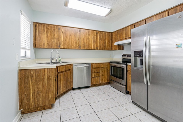 kitchen with brown cabinetry, a sink, stainless steel appliances, light countertops, and under cabinet range hood