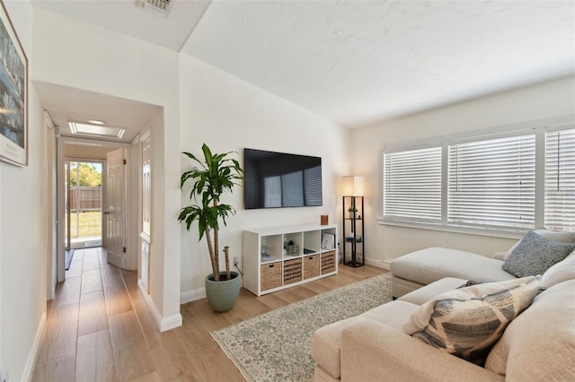 living area with attic access, baseboards, visible vents, and light wood finished floors