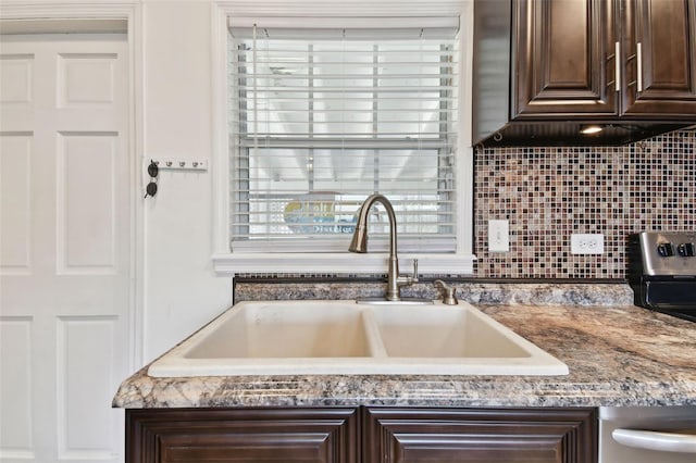 kitchen featuring dark brown cabinetry, stone countertops, backsplash, and a sink