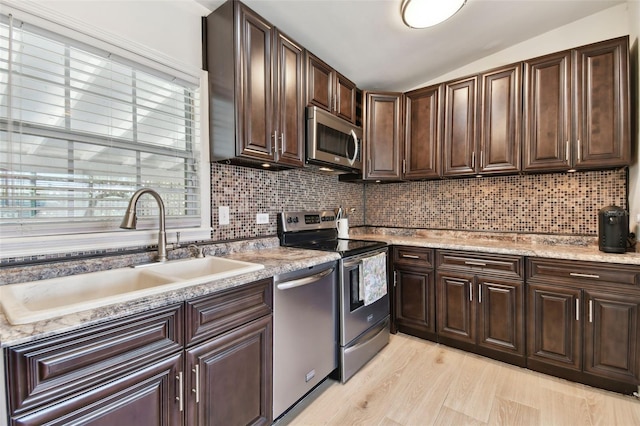 kitchen featuring backsplash, lofted ceiling, light wood-style flooring, stainless steel appliances, and a sink