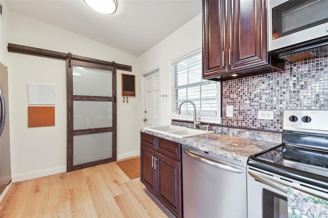 kitchen with vaulted ceiling, decorative backsplash, light wood-style floors, stainless steel appliances, and a sink