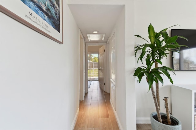 hall featuring attic access, light wood-type flooring, and baseboards