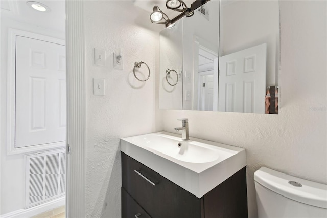 half bathroom with visible vents, toilet, vanity, and a textured wall